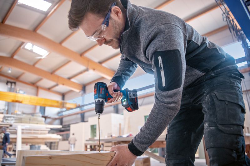 一名佩戴安全设备的人正在使用无绳电动工具在木头上钻孔。.