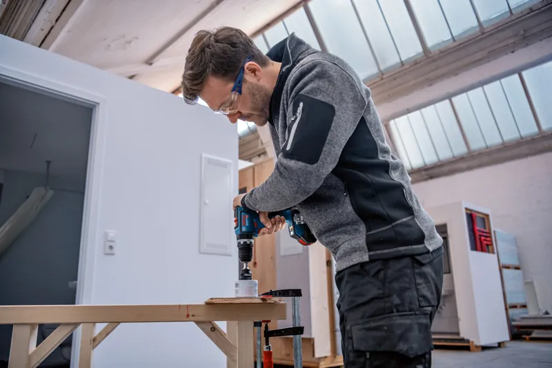 一名佩戴安全设备的人使用无绳电钻在木头上钻孔。.