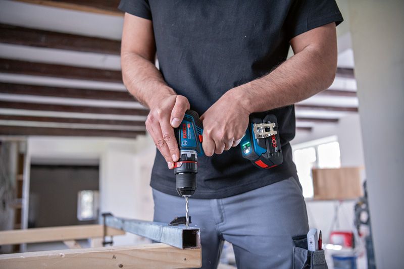 一名工人在车间内使用无绳驱动器在金属梁上钻孔。.