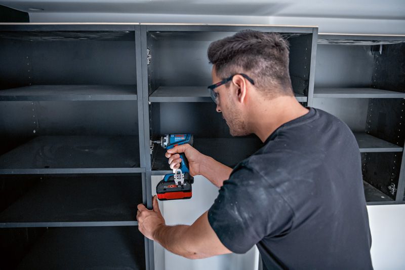 佩戴安全设备的人员使用无绳电钻或起子组装货架。.