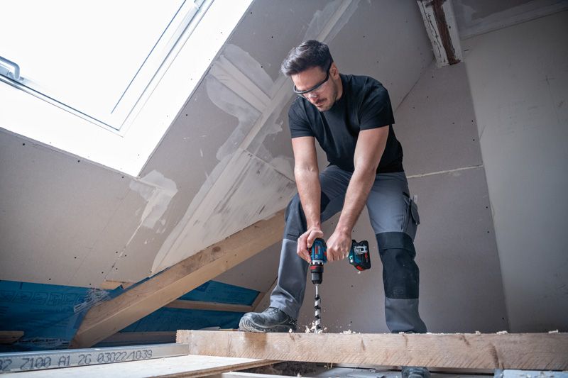 一名佩戴安全设备的人员正在一间尚未完工的阁楼内钻木梁。.