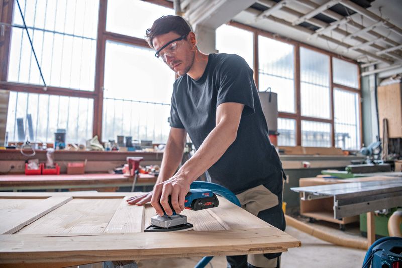 一名佩戴安全设备的人员正在使用无绳轨道砂光机打磨木门。.