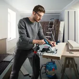 一名佩戴安全设备的人员在车间使用无绳圆锯切割木材。.