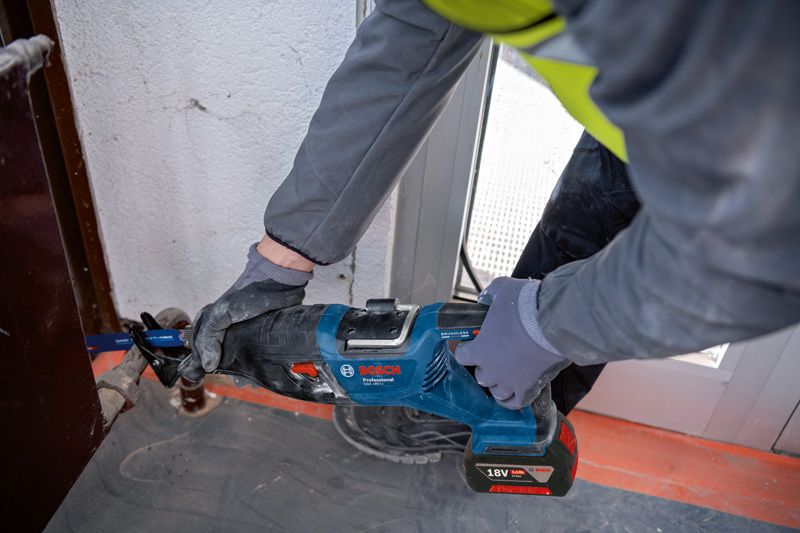 一名佩戴安全设备的人员使用往复锯切割门框附近的金属。.