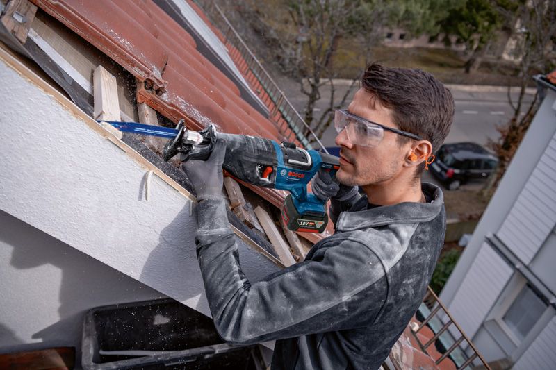 一名佩戴安全设备的人员使用往复锯在屋顶上切割木材。.