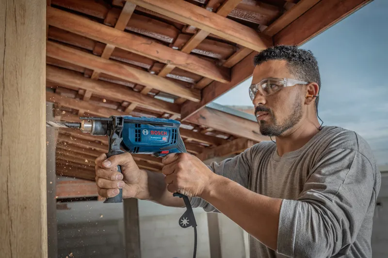 一名佩戴安全设备的人员在木质屋顶下钻入木头。.