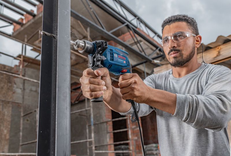 一名佩戴安全设备的人员在建筑工地上钻入金属梁。.