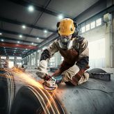 一名佩戴安全设备的人员在工业环境中研磨金属，产生火花。.