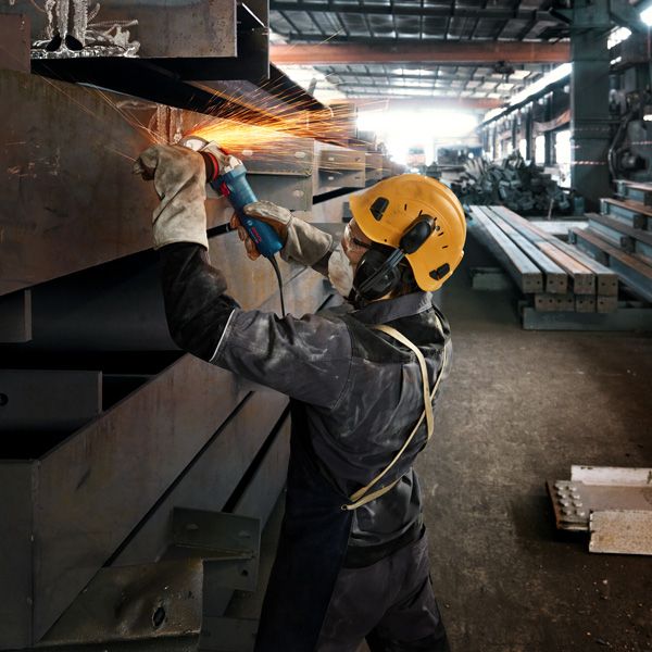 一名佩戴安全设备的人正在研磨金属梁，产生明亮的火花。.
