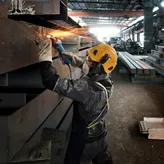 一名佩戴安全设备的人正在研磨金属梁，产生明亮的火花。.