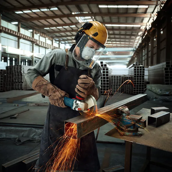 一名佩戴安全设备的人用角磨机打磨金属梁，火花四溅。.