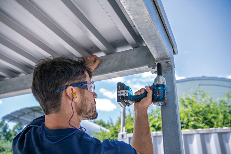 一名佩戴安全设备的人员使用冲击扳手对金属结构进行操作。.