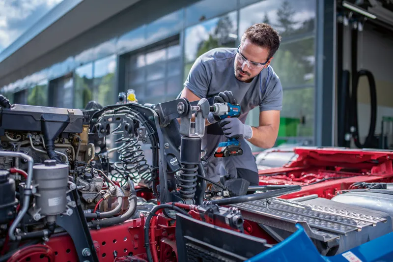 一名佩戴安全设备的人员使用无绳冲击扳手对车辆底盘进行操作。.