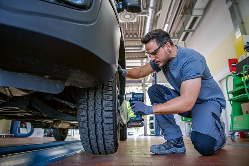 一名佩戴安全设备的人员使用无绳冲击扳手拧紧汽车车轮螺栓。.
