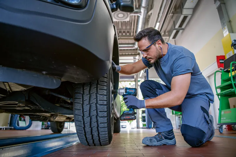 一名佩戴安全设备的人员使用无绳冲击扳手拧紧汽车车轮螺栓。.