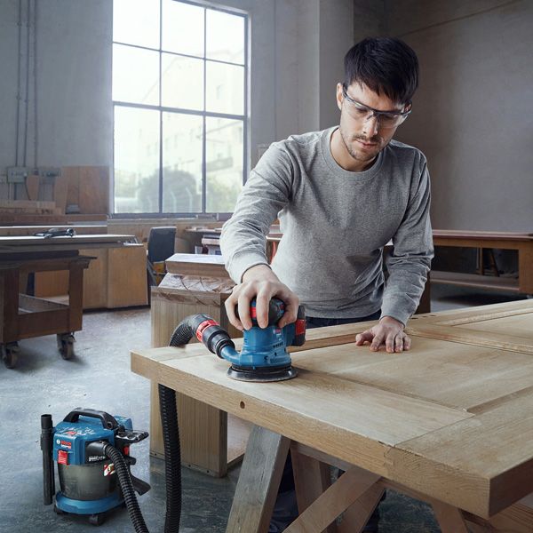 一名佩戴安全设备的人员正在使用连接的轨道砂光机打磨木门。.