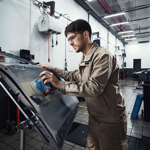 一名佩戴安全设备的人员正在用电动砂光机打磨车门。.