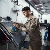 一名佩戴安全设备的人员正在用电动砂光机打磨车门。.