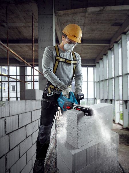 一名佩戴安全设备的人员在正在建造的建筑物中使用电动切割机切割 AAC 砌块。.