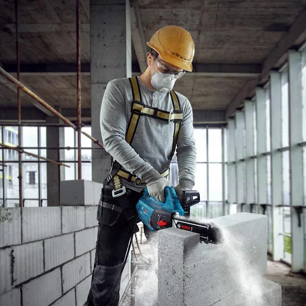 一名佩戴安全设备的人员使用动力切割机切割 AAC 块。.