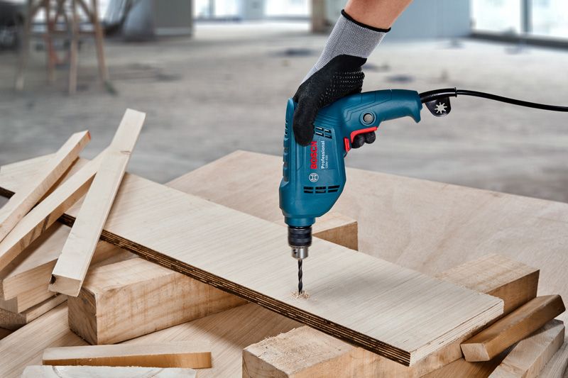 一名佩戴安全设备的人员在木板上钻孔。.