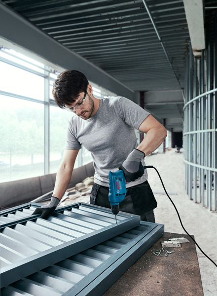 施工现场，一名佩戴安全设备的人员正在将螺丝钻入金属框架中。.