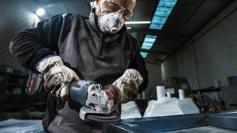 一名佩戴安全设备的人员使用无绳角磨机打磨金属。