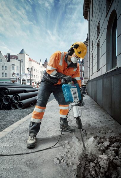 一名佩戴安全设备的人员在城市街道上用断路器破坏路面。.
