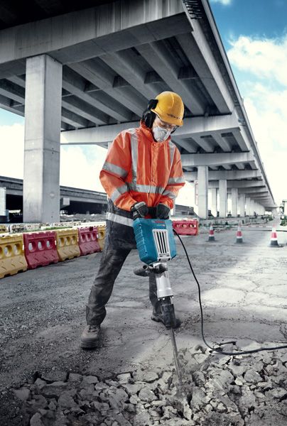 一名身着安全设备的人员在户外使用大型电断路器破碎混凝土。.