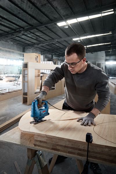 佩戴安全设备的人员使用曲线锯在胶合板上切割出曲线形状。.