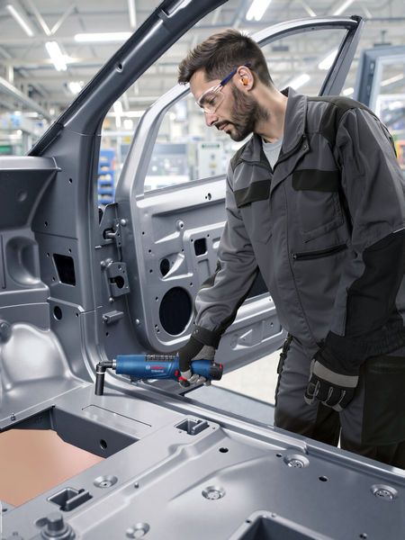 佩戴安全设备的人员在工业环境中使用电动工具对车架进行操作。.