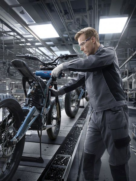 一名佩戴安全设备的工人在工厂里组装摩托车车架。.