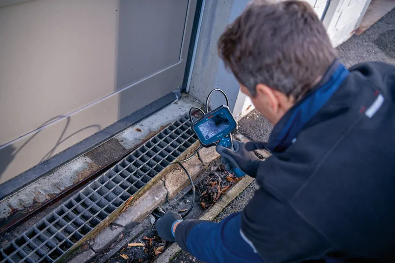 一名佩戴安全设备的人员正在使用检查摄像机检查排水管。.