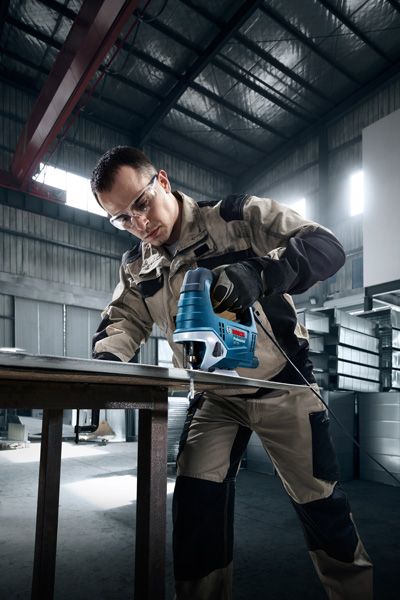 一名佩戴安全设备的人员在车间使用曲线锯切割金属。.