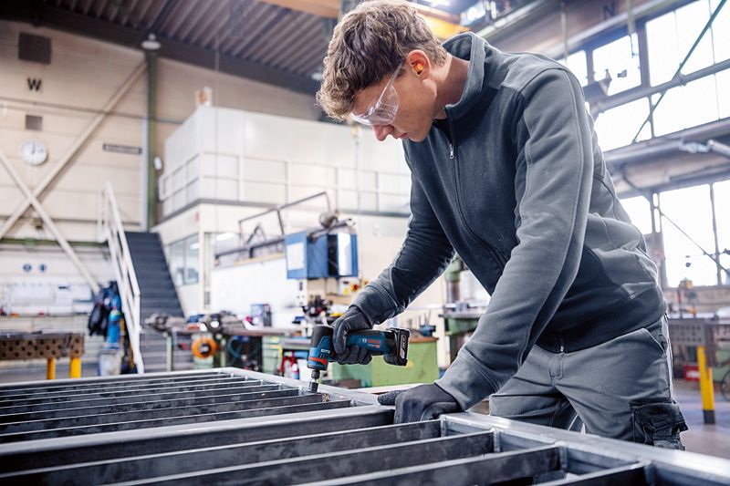 一名佩戴安全设备的人员在金属框架上使用旋转研磨机。.