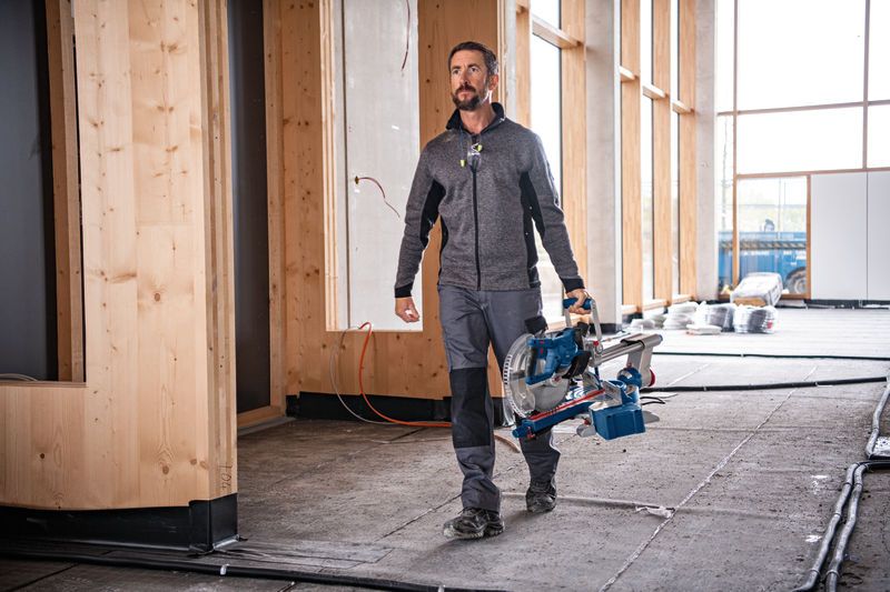 一名佩戴安全设备的人员在施工区域携带无绳斜切锯。.