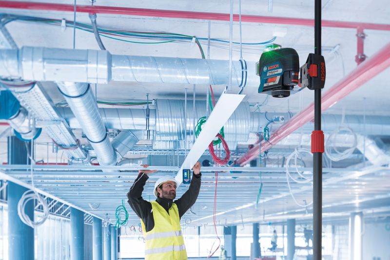 一名佩戴安全设备的人员使用伸缩杆上的激光调平工具安装天花板面板。