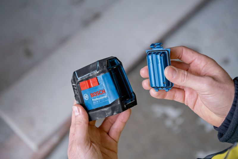 一个人在室内拿着一个蓝色激光调平工具及其电池盒。.