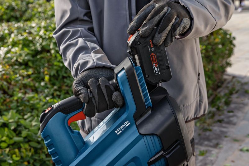 一名佩戴安全装备的人员正在户外将电池装入无绳吹叶机。