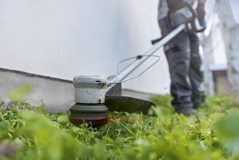 一名佩戴安全设备的人员正在使用无绳割草机沿墙修剪草坪。.