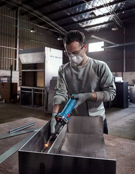 一名佩戴安全设备的人员在工业车间内打磨金属。.