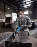 一名佩戴安全设备的人员在工业车间内打磨金属。.