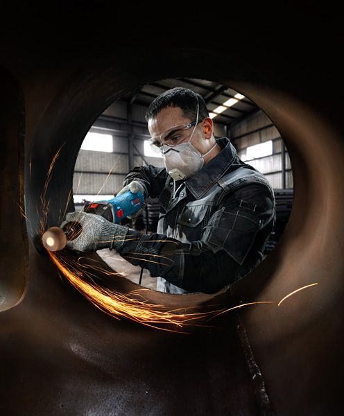 一名佩戴安全设备的人员在一根大管道内研磨金属，产生火花。.