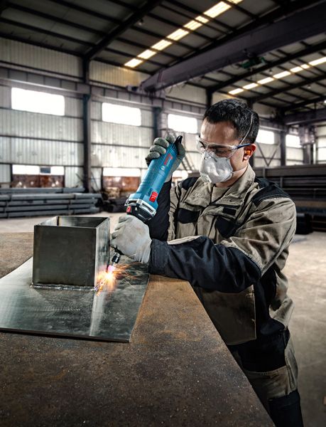 一名佩戴安全设备的人员使用直磨机打磨金属板。.