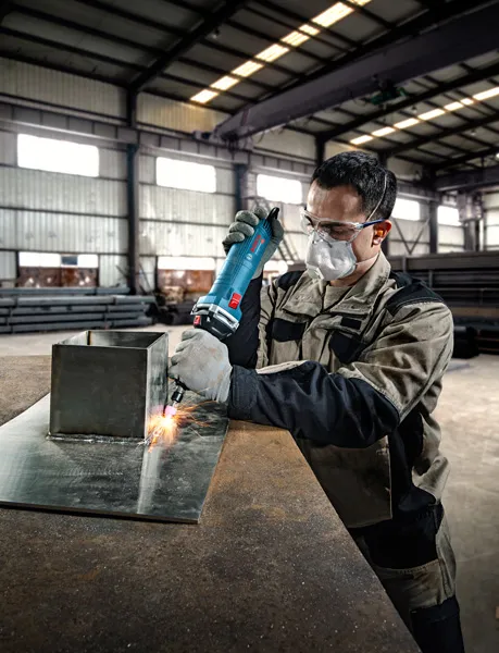 一名佩戴安全设备的人员使用直磨机打磨金属板。.