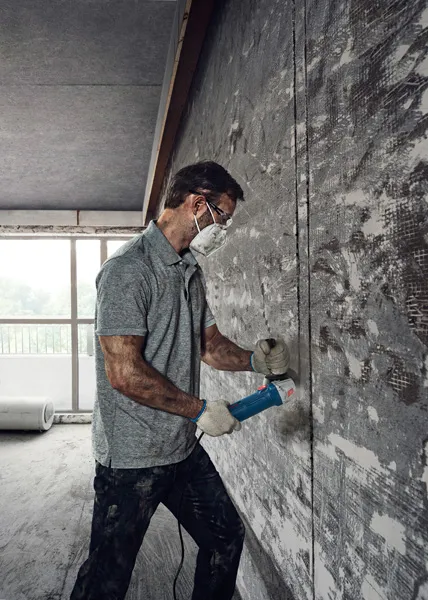 一名佩戴安全设备的人员使用角磨机切割混凝土墙。.