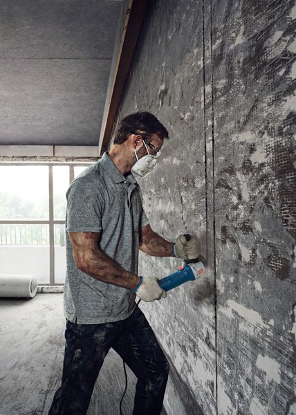 一名佩戴安全设备的人员使用角磨机切割混凝土墙。.