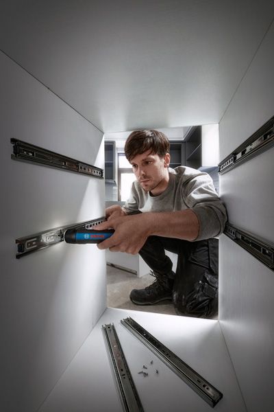 一个人使用无绳螺丝刀在橱柜内安装抽屉滑轨。.