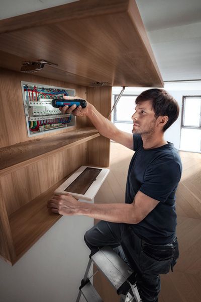 梯子上的人使用无绳螺丝刀对配电盘进行操作。.