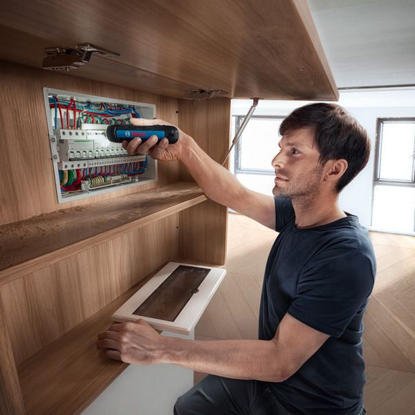 一个人使用无绳螺丝刀固定配电盘中的电线。.